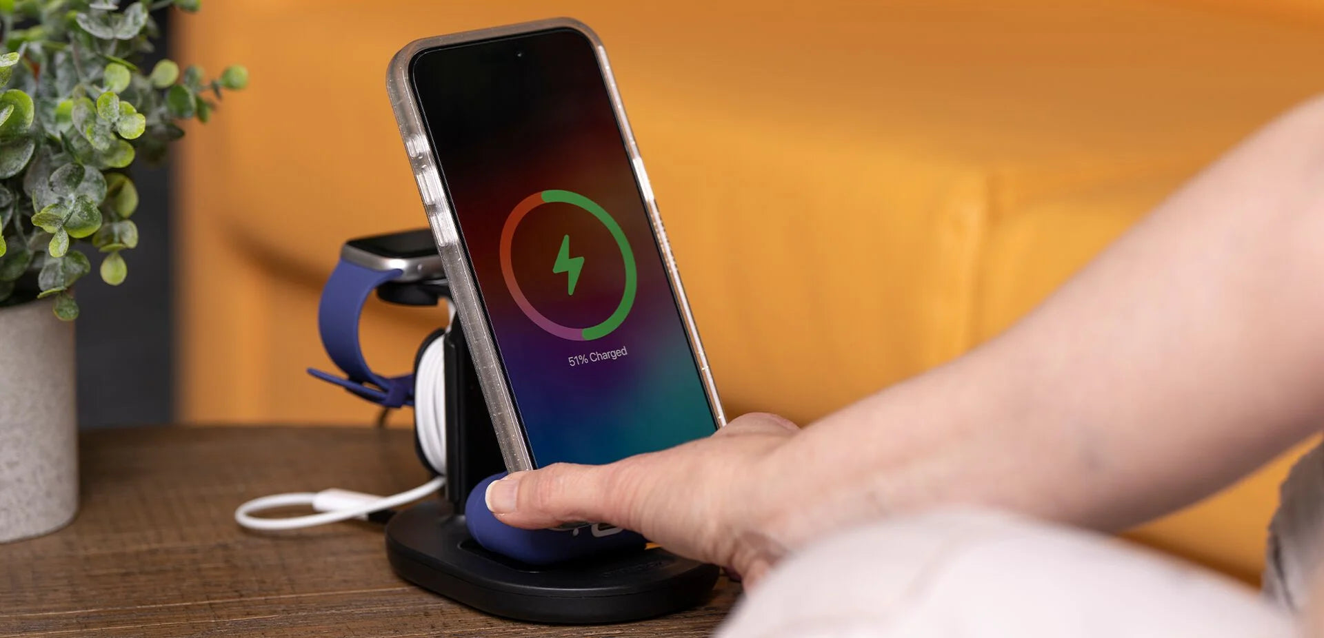 Person using a wireless charging stand with a smartphone on a wooden surface.