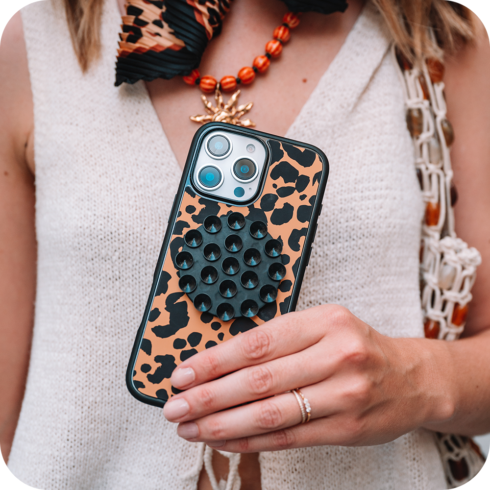 Person holding a phone with a leopard print case, wearing a white sleeveless top.