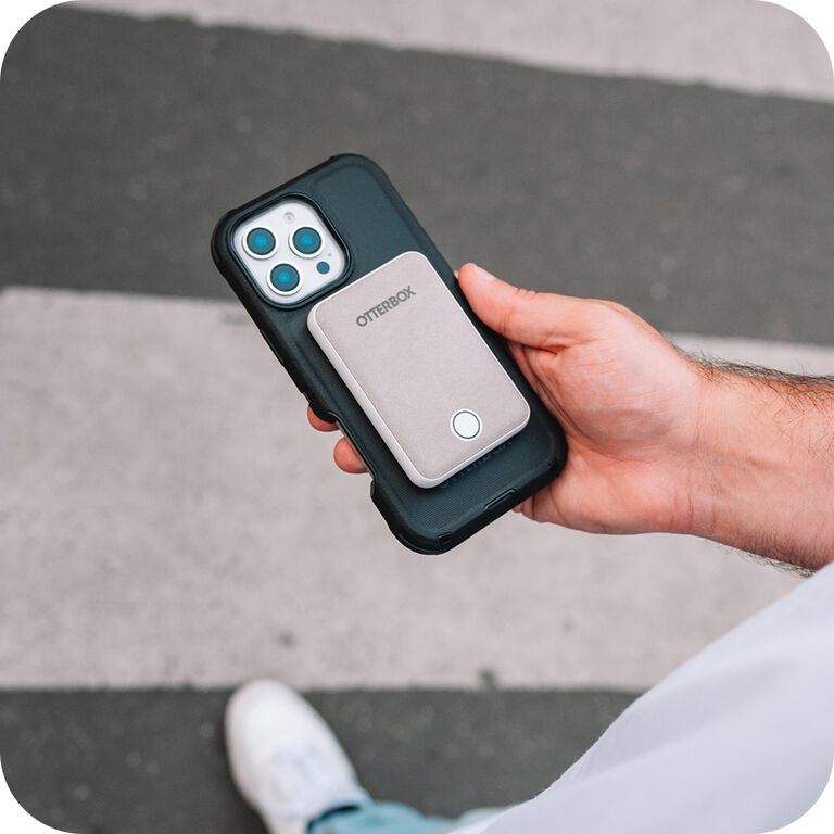 Hand holding a phone case with 'OtterBox' branding magsafe accessory on a pavement background