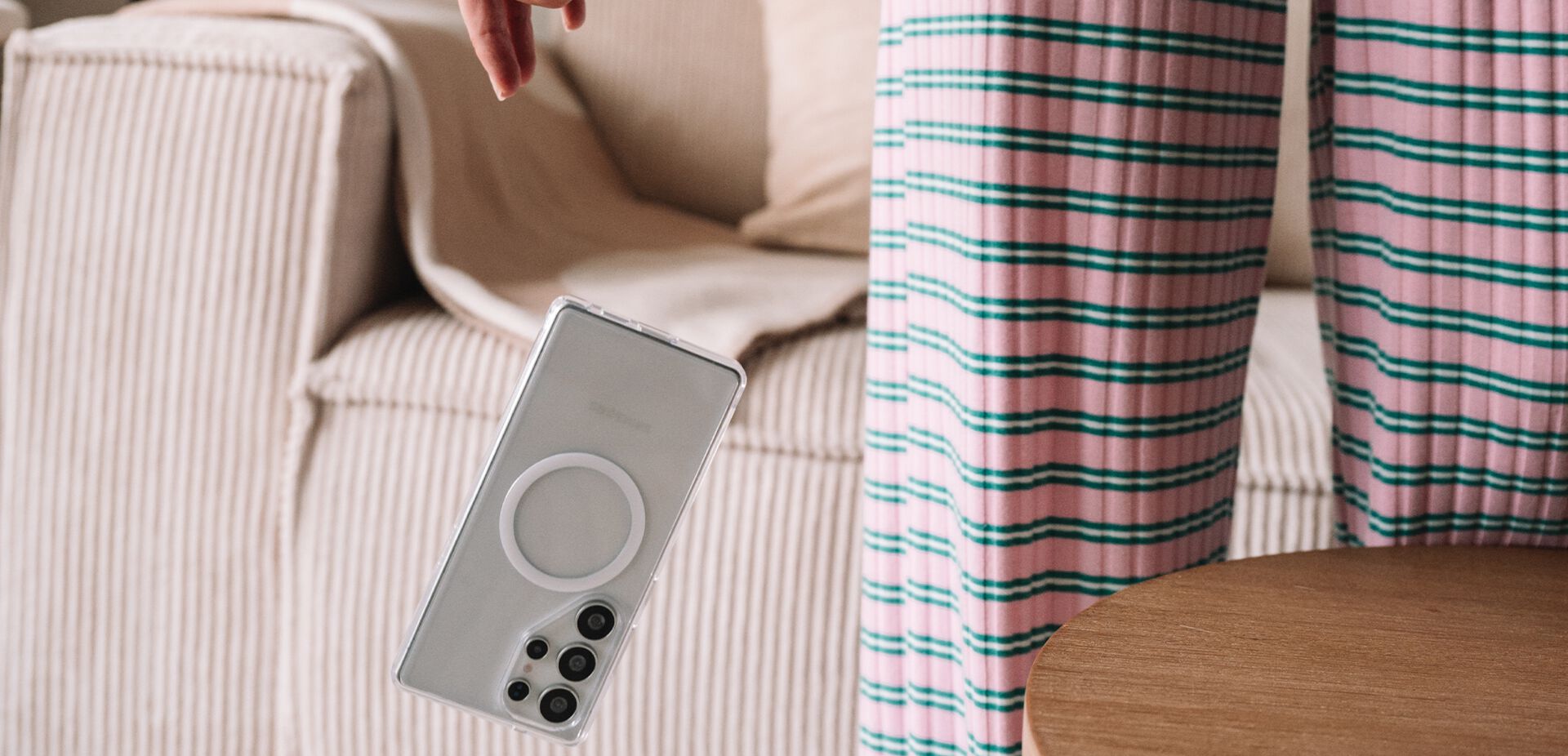 Smartphone held by a hand with a blurred background of a sofa and striped pants.