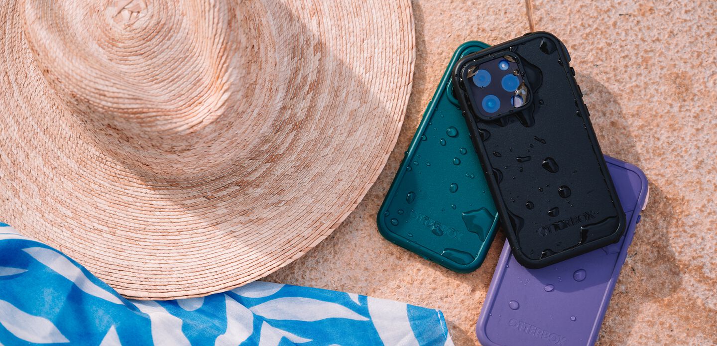 Two phone cases on a textured surface with a straw hat and blue towel.