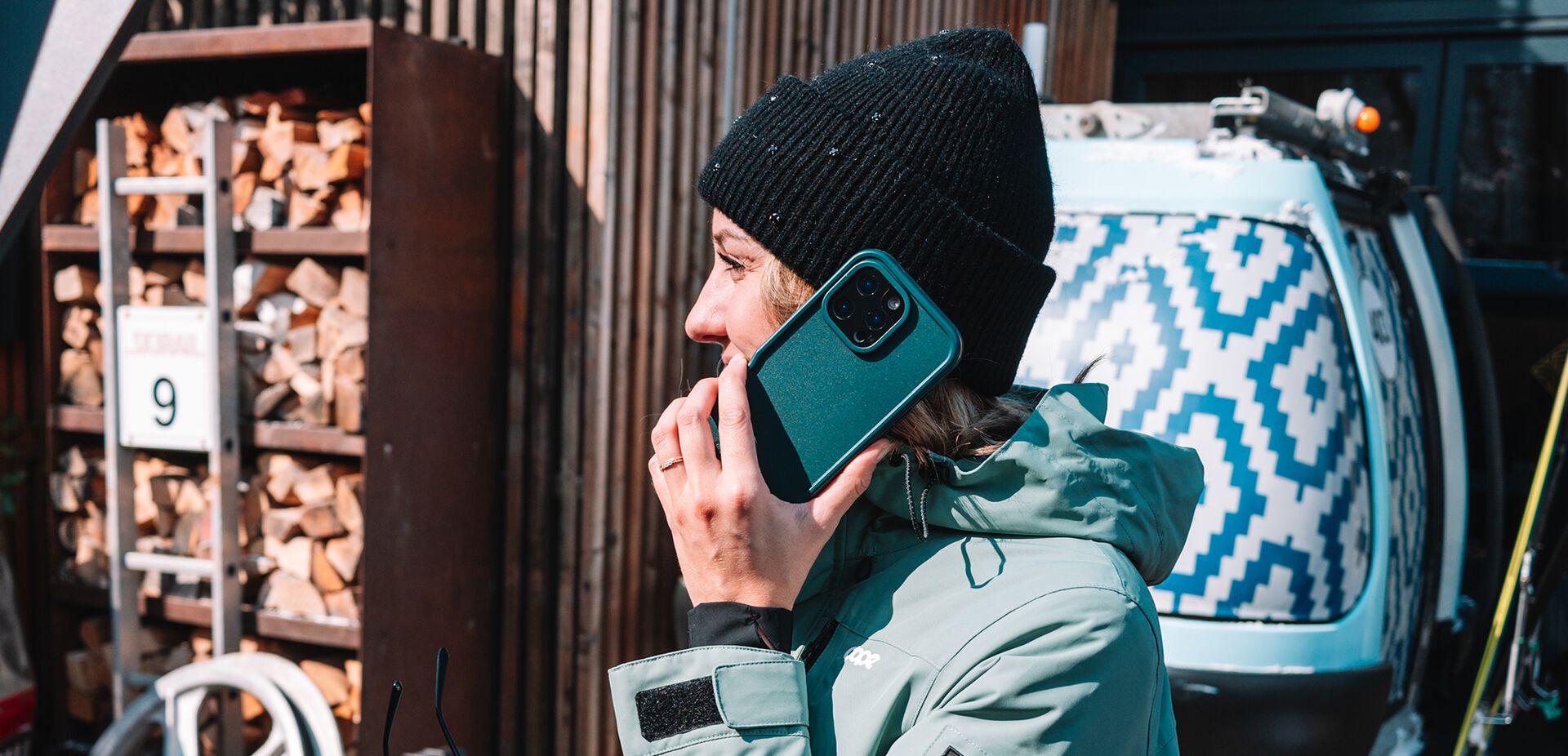 Person talking on a phone with a teal case, standing next to a van with a geometric pattern.